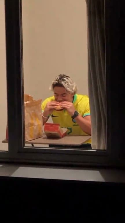 A person has a burger behind a glowing apartment window at night.